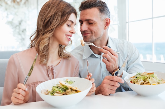 Foto des erwachsenen romantischen Paares, das Abendessen und das Essen von Salaten beim Ausruhen im Stadtcafé am sonnigen Tag isst