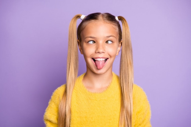 Foto des fröhlichen lustigen lächerlichen Mädchens, das ihre Zunge herausstreckt und Augen macht, die einander isolierte violette Pastellfarbenwand betrachten