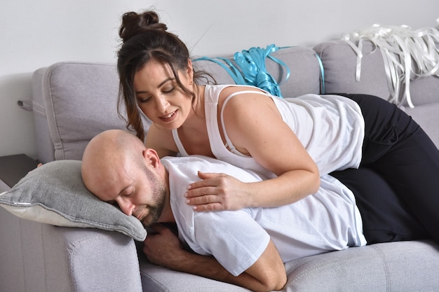 Foto des fröhlichen romantischen kaukasischen Familienpaares lächelnd und umarmend, während auf dem Sofa zu Hause sitzend. Mann und Frau verliebt