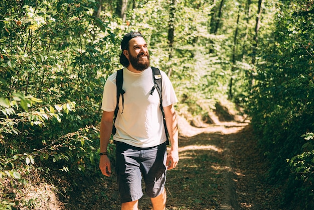 Foto des jungen bärtigen Mannes, der im Wald während der Sommerzeit, Reisekonzept wandert.