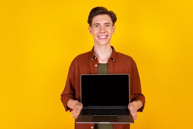 Foto des jungen fröhlichen Mannes zeigt Laptop-Promo-Angebotsmanager, der über gelbem Farbhintergrund isoliert ist