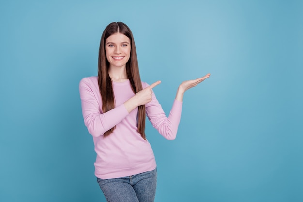 Foto des jungen Mädchens glückliches positives Lächeln Punktfinger-Produkt-Promo-Angebotsverkauf einzeln auf blauem Farbhintergrund