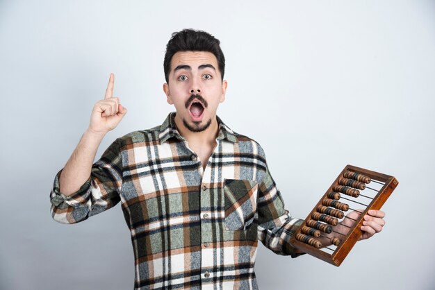 Foto des jungen Mannes, der hölzerne Zählperlen über weißer Wand hält.