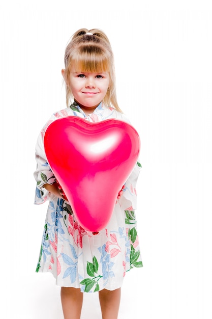 Foto des kleinen Mädchens in einem Kleid mit Blumendruck hält einen roten herzförmigen Ballon