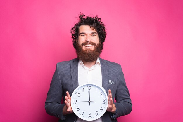 Foto des lächelnden bärtigen Mannes, der lässigen Anzug hält weiße Uhr hält