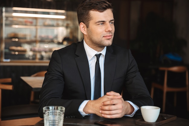 Foto des schönen jungen Geschäftsmannes in der formellen Kleidung drinnen im Café.