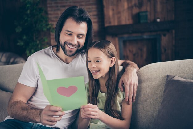 Foto des schönen kleinen entzückenden Mädchens und des hübschen jungen Papas sitzen auf bequemem Sofa