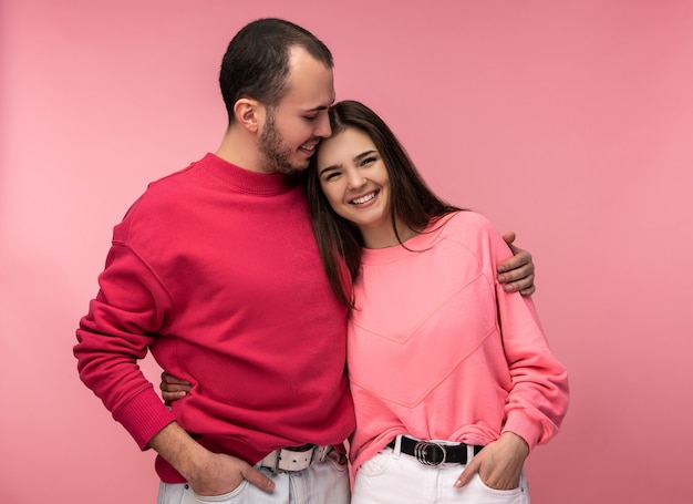 Foto des süßen Paares umarmen sich und lächeln. Mann und Frau sind verliebt, isoliert über rosa Hintergrund.
