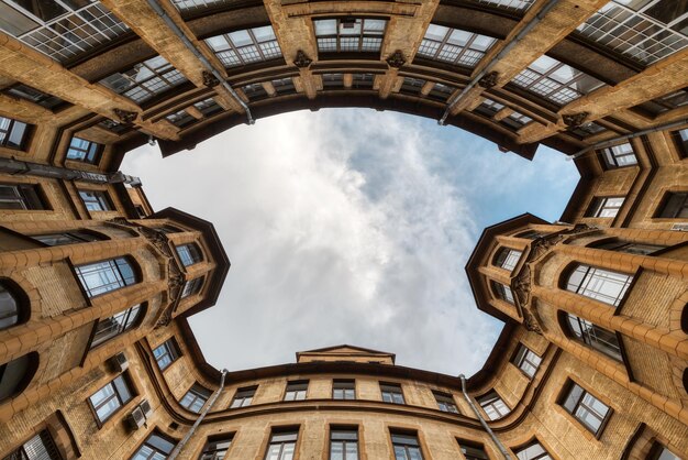 Foto des symmetrischen Hofes im Wohnhaus vom historischen Zentrum von Sankt Petersburg in Russland. Blauer bewölkter Himmel. Die Fassade mit zwei Erkern ist mit Skulpturen von Wasserspeiern verziert.