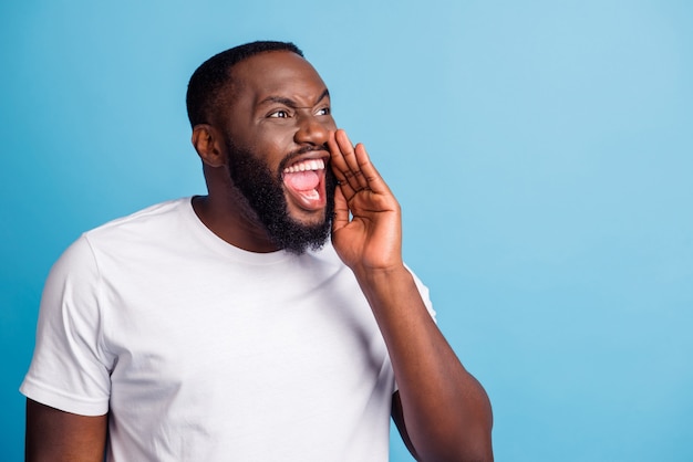 Foto des wütenden afrikanischen Mannes Hand offener Mund schreien Blick leerer Raum tragen weißes T-Shirt auf blauem Hintergrund