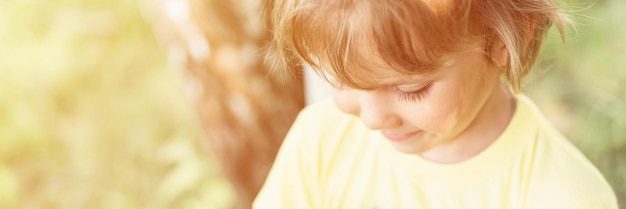 Foto desenfocada de desenfoque de movimiento de retrato sonriente niño soleado caucásico niño sincero con cabello rubio largo ondulado o rizado y luz solar en la cara en el bosque de la naturaleza al aire libre. bandera. llamarada