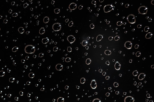 Foto detallada: las gotas de agua de lluvia detrás del vidrio parecen burbujas en un líquido negro. Fondo húmedo abstracto.