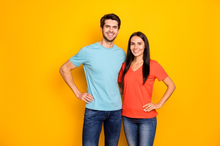 Foto de divertido encantador dos personas pareja chico y dama abrazándose las manos a los lados uno mejor ropa de equipo casual azul naranja camisetas jeans aislado sobre pared de color amarillo