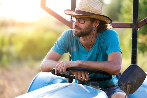 Foto do agricultor jovem hippie no trator, procurando sua colheita no jardim.