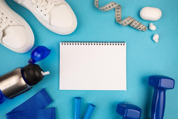 Foto do caderno em branco halteres azuis tapete de exercícios azul tênis branco e outros equipamentos esportivos O conceito de esporte fitness yoga perda de peso estilo de vida saudável