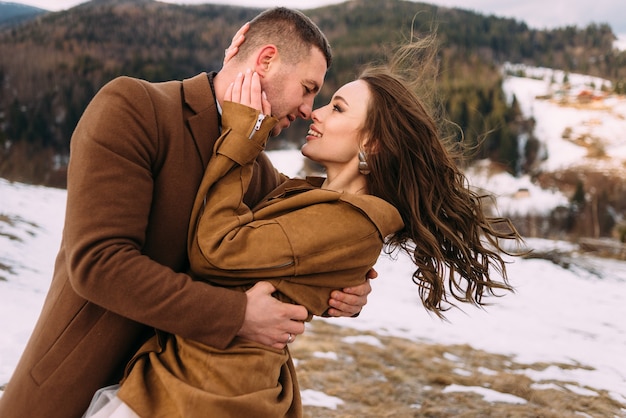 foto do close up de uma noiva e um noivo acariciando contra o pano de fundo das montanhas de inverno. recém-casados calorosamente vestidos se abraçam.