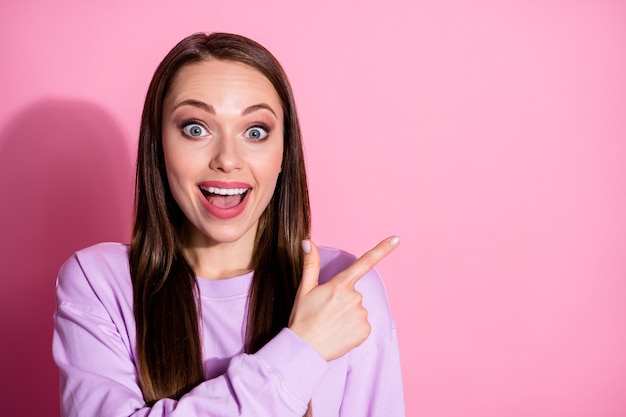 Foto do close up de uma senhora atraente e animada com os dedos diretos ao lado do espaço vazio mostrar a novidade banner shopping boca aberta usar suéter roxo casual isolado fundo de cor rosa pastel