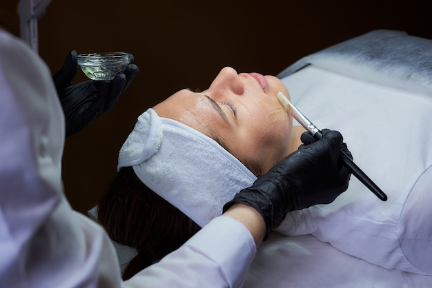 foto do cosmetologista que aplica loção de aquecimento no rosto da mulher.