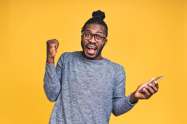 Foto do homem negro afro-americano muito feliz, sabendo que ele se tornou o vencedor de algo tão regozijante, desfrutando de informações de notícias enquanto isolado sobre o fundo amarelo.