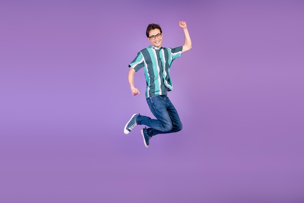Foto do lado do perfil de corpo inteiro do jovem saltador alegrar-se com o sucesso da vitória isolado sobre o fundo de cor violeta