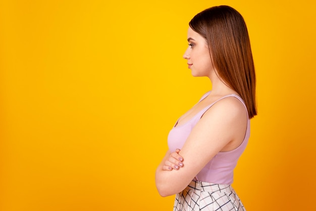 Foto do lado do perfil de uma jovem encantadora, mãos dobradas, com aparência inteligente, espaço vazio isolado sobre fundo de cor amarela