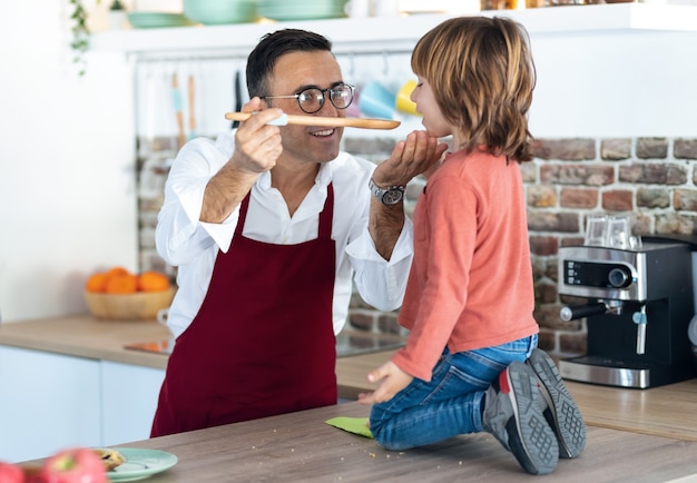 Foto do pai bonito cozinhando e deixando o filho provar a comida na cozinha de casa.