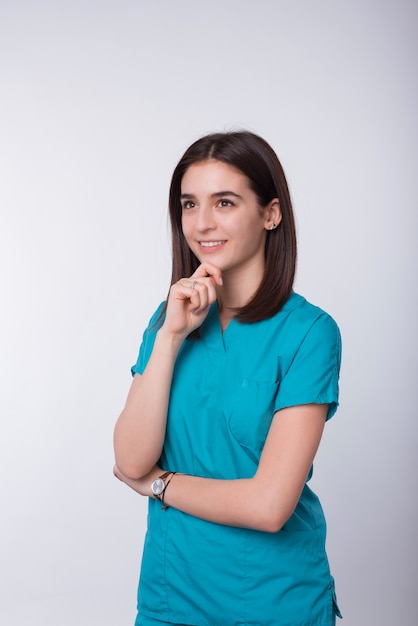 La foto de la doctora sonriente joven está haciendo gesto de pensamiento en el espacio en blanco.