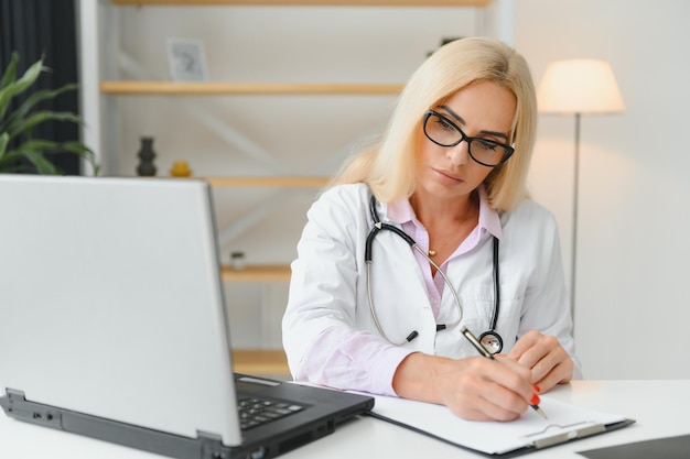 Una foto de una doctora trabajando sentada en el escritorio frente a una laptop