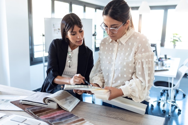 Foto de dos hermosas mujeres jóvenes diseñadoras que trabajan en un proyecto de diseño mientras eligen materiales en la oficina.