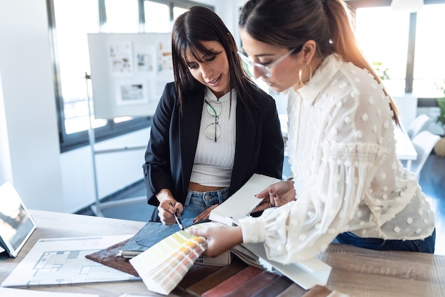 Foto de dos hermosas mujeres jóvenes diseñadoras que trabajan en un proyecto de diseño mientras eligen materiales en la oficina.