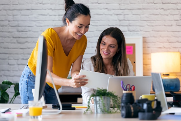 Foto de dos jóvenes empresarias hablando y revisando su último trabajo en la tableta digital en la oficina.