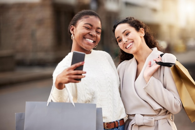 Foto de dos mujeres jóvenes tomándose selfies mientras compran en un entorno urbano