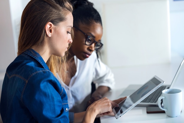 Foto foto de dos mujeres de negocios bastante jóvenes que trabajan junto con tableta digital en la oficina.