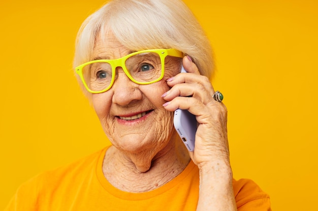 Foto einer alten Dame im Ruhestand, die am Telefon in gelben Gläsern telefoniert, Nahaufnahme von Emotionen
