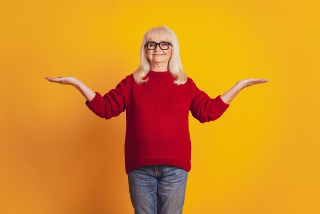 Foto einer alten netten Dame, die offene Palmen hält und Varianten vorschlägt, kopieren den gelben Studiohintergrund