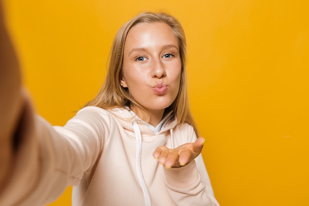 Foto einer blonden Frau 16-18 mit Zahnspange, die lächelt und ein Selfie macht, isoliert auf gelbem Hintergrund