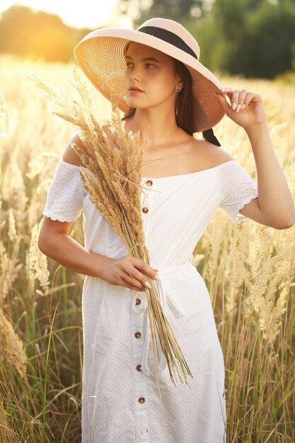 Foto einer charmanten kaukasischen Frau mit Strohhut, die am Sommertag auf einem Weizenfeld ruht