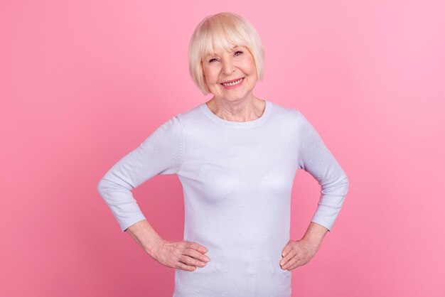 Foto einer charmanten Seniorin mit guter Laune, die Hände auf der Taille zuversichtlich isoliert über rosafarbenem Hintergrund