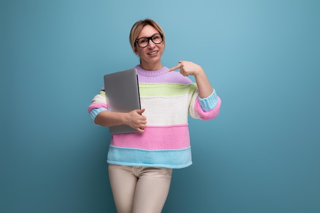 Foto einer erfolgreichen blonden Freiberuflerin in einem gestreiften Pullover mit einem Laptop auf einem Blau