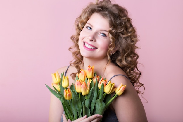 Foto einer Frau mit einem glücklichen Lächeln auf ihrem Gesicht, das Blumen in ihren Händen hält, die im rosa Hintergrund genommen werden.