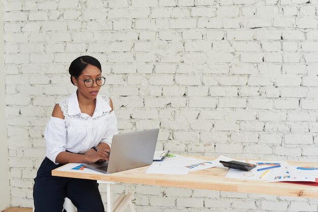 Foto einer fröhlichen, fröhlichen Mischlingsfrau im weißen Hemd, die Training oder Konferenz mit Laptop hält.