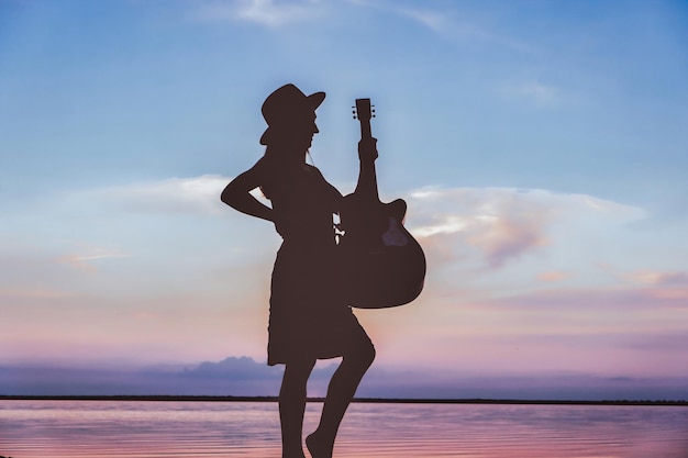 Foto einer glücklichen Frau mit akustischer Gitarre, die überglücklich war, isolierte lebendige blaue Sonnenuntergangsfarbe Hintergrund