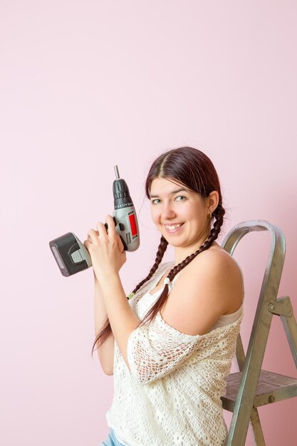 Foto einer glücklichen Frau mit Bohrgerät in der Nähe von Leitern