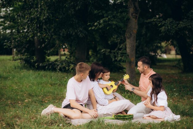 Foto einer großen Familie, fünf Personen, drei kleine Kinder, sitzen auf der Bank, am Tisch, entspannen sich, köstliches Abendessen, essen Sandwich, Äpfel, Salat, Generation, sonniges Wochenende, Komfort, Zuhause, Park, Hinterhof im Freien