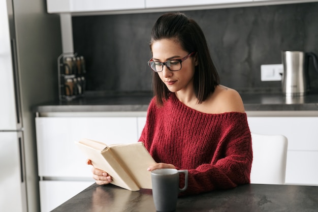 Foto einer hübschen Frau drinnen zu Hause am Küchenlesebuch.