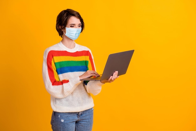 Foto einer hübschen jungen Dame, die am Laptop arbeitet und eine blaue Jeans trägt, die auf hellgelbem Hintergrund isoliert ist