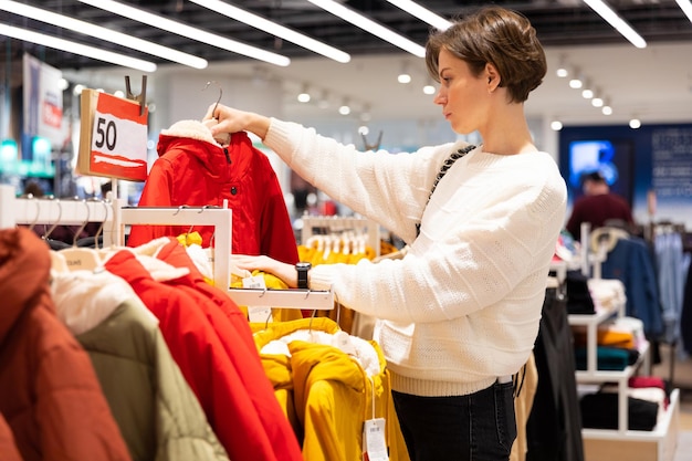 Foto einer jungen attraktiven brünetten frau mit kurzem haarschnitt in einem weißen pullover wählt stilvoll und