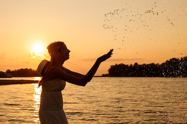 Foto einer jungen Frau bei Sonnenuntergang ist eine Seitenansicht einer schlanken schönen Blondine in einem Sommerkleid...