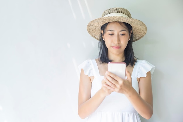 Foto einer jungen Frau, die in einem weißen Kleid und einem Strohhut glücklich ist. Positives Lächeln verwendet ein Smartphone