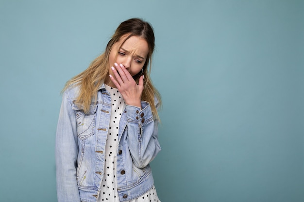 Foto einer jungen müden, müden, schönen blonden Frau mit aufrichtigen Emotionen, die eine blaue Jeansjacke trägt